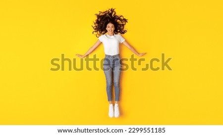 Beauty Offer. Pretty Young Lady Lying On Floor Posing Smiling At Camera Over Yellow Studio Background, Top View. Full Length Shot Of Happy Woman Wearing White T-Shirt And Skinny Jeans Royalty-Free Stock Photo #2299551185