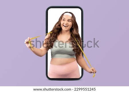 Smiling young caucasian woman plus size in sportswear and measuring tape on smartphone screen isolated on violet studio background. Body care, sports, app for weight loss and fitness