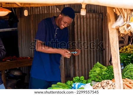 excited young african man taking picture of fresh vegetables in a local marketplace