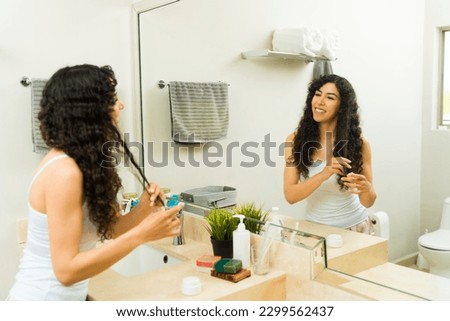 Cheerful woman smiling in the bathroom using a conditioner treatment on her curly hair getting ready in the morning 