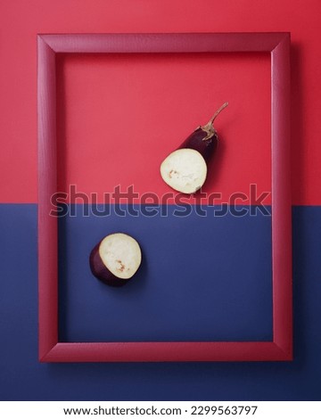 Cut in half eggplant in wooden picture frame on red and blue background