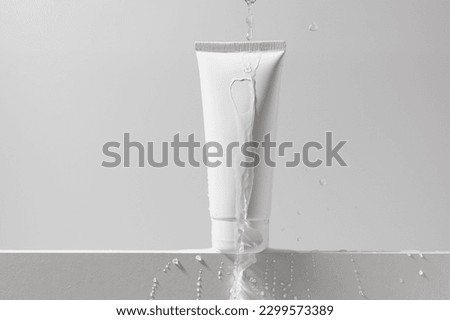 White mockup of a tube of cream with a stream of water and drops on an isolated background. Daily skincare and body care routine. Template for beauty products Royalty-Free Stock Photo #2299573389