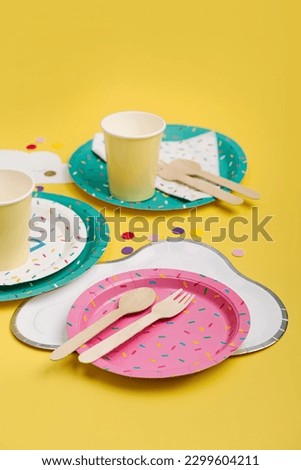 Cute paper party plates and cups for themed kids party on yellow background. Birthday party decorations and props in bright colors. Set of holiday disposable tableware for party or picnic.  Royalty-Free Stock Photo #2299604211