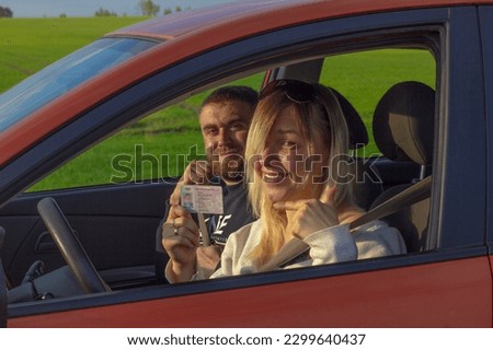 Holding in hand obtained driver's license woman smiling joyfully while sitting in the car. A woman passed a driving test with an instructor. The woman got her driver's license and is very happy. Royalty-Free Stock Photo #2299640437