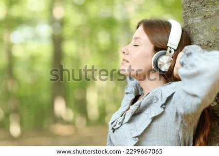 Side view portrait of a happy woman relaxing listening music in a forest