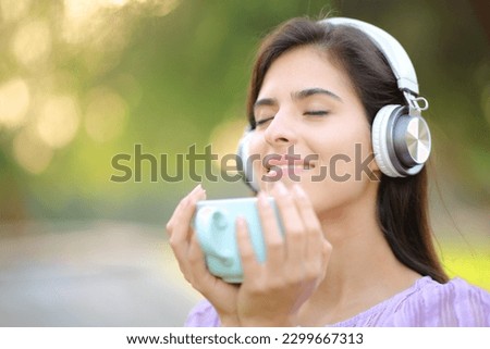 Relaxed woman wearing headphone listening music and drinking coffee in a park