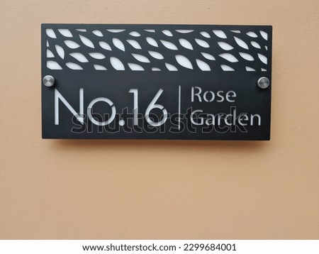 Modern acrylic house number plate on brown wall background.