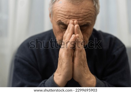 Please, Lord. Nervous worried aged Caucasian man praying on couch at home. Stressed white European senior citizen sitting on sofa, begging for forgiveness or asking God for help in difficult situation Royalty-Free Stock Photo #2299695903