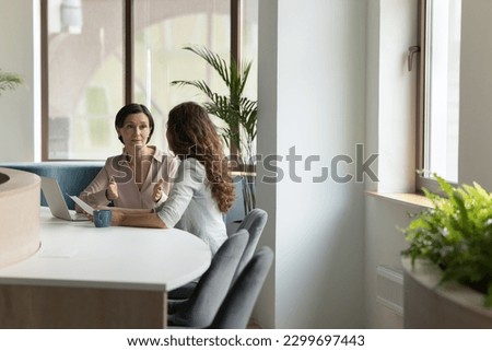 Serious mature female executive manager lead formal meeting with company client in office, make commercial offer, share information, convince customer to buy services met in modern workspace. Business Royalty-Free Stock Photo #2299697443