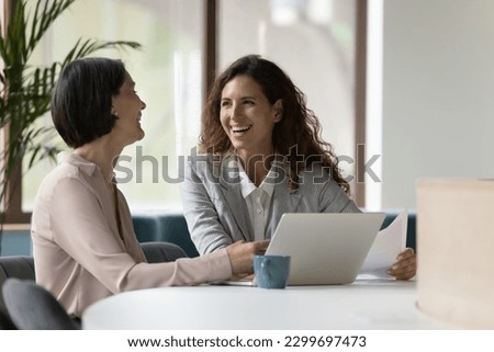 Two happy businesswomen, office employees work in office, laughing, joking during workflow, share creative ideas, solution feel satisfied with corporation, engaged in teamwork. Negotiation, business Royalty-Free Stock Photo #2299697473