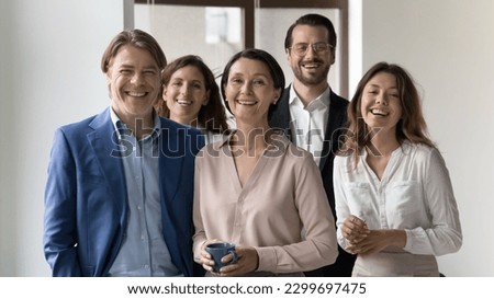 Five young and mature businesspeople, successful, well-dressed staff standing as team in modern office smiling looking at camera. Business leadership, growth, professional occupation people portrait