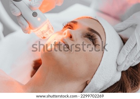 Photo from the studio of cosmetology, demonstrating the process of led therapy and facial skin care. A woman undergoes a procedure in a beauty salon. Beautician in white gloves use Royalty-Free Stock Photo #2299702269