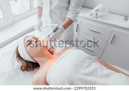 The beautician conducts light therapy of the face in a beauty clinic using an LED device. Procedure improves microcirculation and stimulates collagen production, and increases skin tone and elasticity Royalty-Free Stock Photo #2299702351