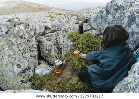 A tourist girl on a hike drinks coffee in the mountains, brew a hot drink in nature, take cover with a warm sleeping bag, a cool morning in the taiga, breakfast in nature. High quality photo