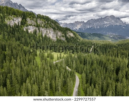 Aerial shot of a curvy road in a forest near the giau pass in the dolemite mountain range. Winding road in mountain valley under rainy clouds.