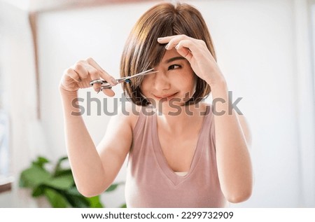 Portrait of beauty asian woman has scissors hand cutting hair during lockdown of coronavirus. Girl have new hairstyle haircut, DIY hair cut during covid stay home, new normal lifestyle barber concept Royalty-Free Stock Photo #2299732909