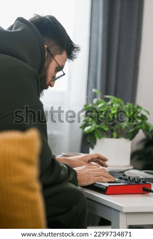 Man recording electronic music track with portable midi keyboard on laptop computer in home studio. Producing and mixing music beat making and arranging audio content with professional audio devices