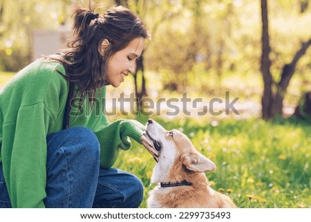 Portrait of a caucasian woman in green sweater and with corgi dog sitting on a grass in a park during summer girl and her corgi dog looking at each other