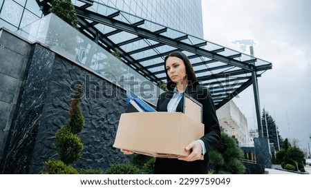 A white-collar worker holds a cardboard box, their expression reflecting the stress of unemployment and workloss. Royalty-Free Stock Photo #2299759049