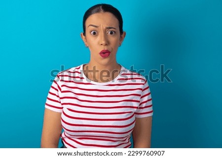 woman wearing striped T-shirt over blue studio background expressing disgust, unwillingness, disregard having tensive look frowning face, looking indignant with something.