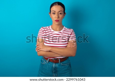 Picture of angry woman wearing striped T-shirt over blue studio background looking camera.