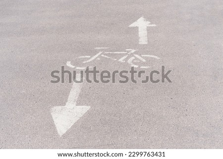 This photo features a detailed close-up of a bicycle sign painted on the asphalt pavement. The sign indicates a bicycle lane on the sidewalk and features a white silhouette of a bike
