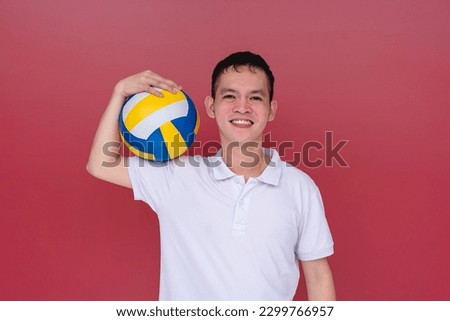 A young asian volleyball instructor or coach holding a volley ball. Isolated on a red background.