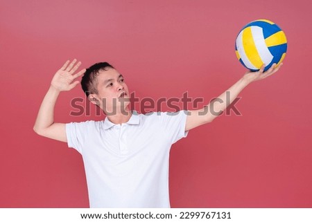 A sporty and athletic young man doing a volleyball serve position with the ball raised on one hand. Isolated on a red background.