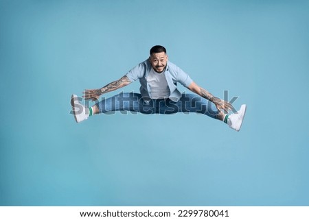 Full length of crazy overjoyed asian man jumping in air with raised legs, feeling energetic and lively. indoor studio shot isolated on blye background 