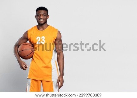 Portrait of confident smiling African American man, professional basketball player holding ball isolated on white background. Sportsman wearing orange basketball uniform looking at camera, copy space Royalty-Free Stock Photo #2299783389