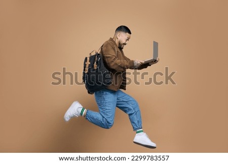 Profile photo of sporty active asian guy jumping with laptop computer, enjoying online education isolated brown colour background 