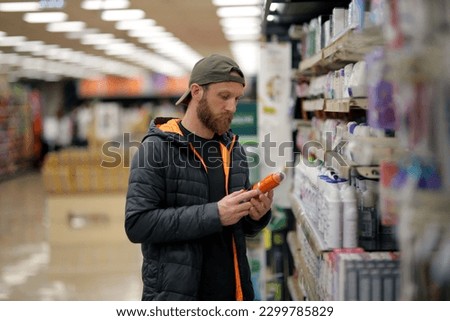 A bearded caucasian man customer is interested in a deodorant spray bottle at the grocery store, supermarket Royalty-Free Stock Photo #2299785829