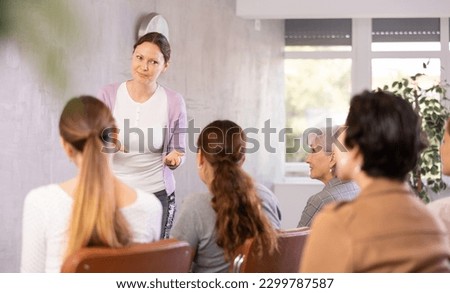 Young woman qualified coach speaks to small audience of listeners and talks about upcoming tasks for volunteers and campaign policy Royalty-Free Stock Photo #2299787587