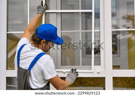 An experienced worker quickly and professionally puts a net on a plastic window in the summer. Wizard installs the mesh in the plastic fasteners on the white window Royalty-Free Stock Photo #2299829123