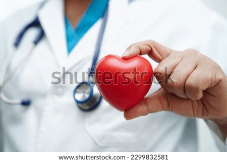 Asian woman doctor holding red heart for health in hospital.