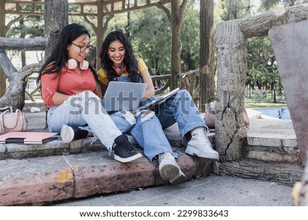 two young latin women students using laptop sitting on bench park in Mexico Latin America, hispanic girls studying  Royalty-Free Stock Photo #2299833643