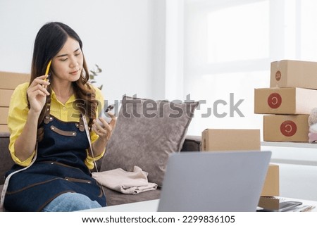 Young asian online seller businesswoman working shipping at home looking at mobile phone for online orders and thinking about her business future, good for online seller business concept.