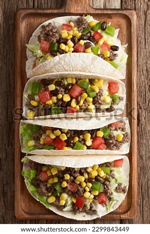 Flour tortillas filled with mincemeat and vegetables, lettuce, tomato, corn, green bell pepper and beans, served on wooden board, photographed overhead (Selective Focus on the top of the tortillas)