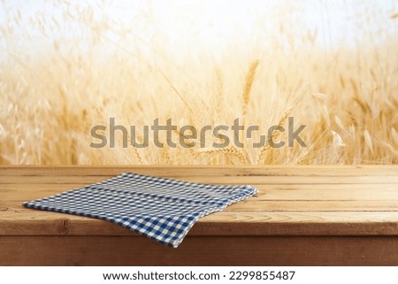 Empty wooden table with tablecloth over wheat field blurred background. Shavuot holiday mock up for design and product display Royalty-Free Stock Photo #2299855487