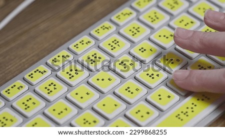 Close-up of a computer keyboard with braille. A blind girl is typing words on the buttons with her hands. Technological device for visually impaired people. Tactilely touches bumps on the keys Royalty-Free Stock Photo #2299868255