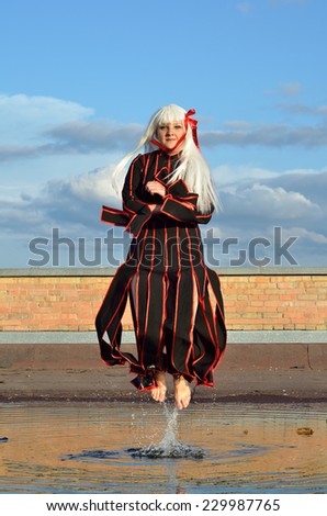 A teenage girl is kiting under the puddle in the roof against the sky. She is wearing an anime dress and a wig.