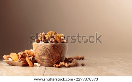 Dried fruits and nuts on a beige ceramic table. The mix of nuts, apricots, and raisins in a wooden bowl. Copy space. Royalty-Free Stock Photo #2299878393