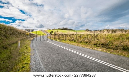 Winding empty road going up-hill through Adelaide Hills farmland during winter season, South Australia Royalty-Free Stock Photo #2299884289
