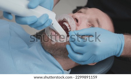 Close up: Doctor scans the teeth of a male patient in the medical office of clinic. The dentist holds in his hand a manual 3D scanner for the jaw and mouth. Dental health. Creates a 3D model of teeth Royalty-Free Stock Photo #2299891159
