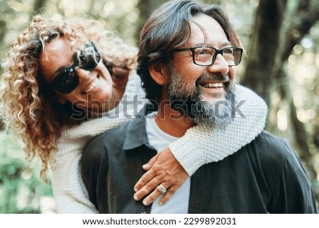 Youthful mature people enjoying weekend activity together. Man carrying woman in piggyback and having fun with love. Man wearing glasses and woman hugging him. Happy life and relationship. Together Royalty-Free Stock Photo #2299892031