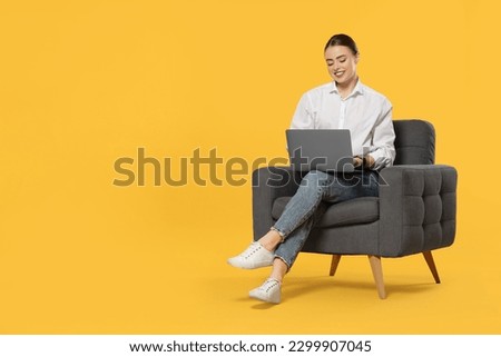 Happy woman with laptop sitting in armchair on orange background. Space for text