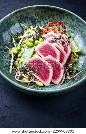 Modern style traditional Japanese gourmet seared tuna fish steak tataki with soba noodles and stir-fried vegetables served as close-up on a Nordic design bowl Royalty-Free Stock Photo #2299909991