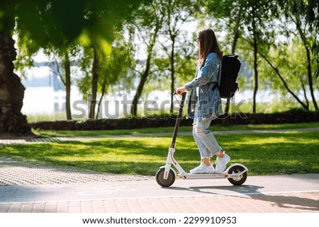 Young female legs on an electric scooter. Beautiful woman rides an electric scooter in the park on a sunny day. Ecological transport. Active lifestyle. Royalty-Free Stock Photo #2299910953