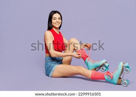 Full body side view happy fun cool young latin woman wearing red casual clothes rollerblading sit laces up rollers isolated on plain pastel purple background. Summer sport lifestyle leisure concept
