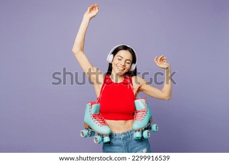 Young fun happy latin woman wear red casual clothes hold in hand rollers listen to music in headphones dance isolated on plain pastel purple background studio. Summer sport lifestyle leisure concept
